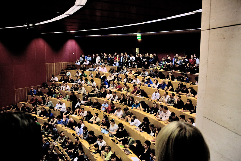 Das Bild zeigt einen vollen Hörsaal mit vielen Studierenden aus der Seitenperspektive